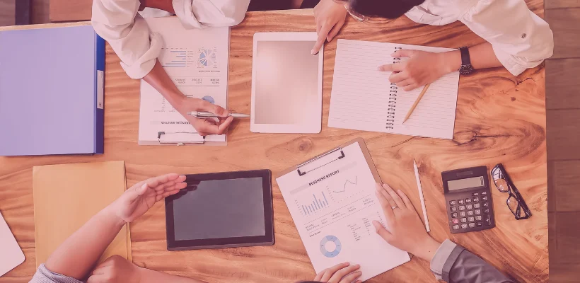 Na stole leżą dokumenty marketingowe, a osoby je przeglądają
