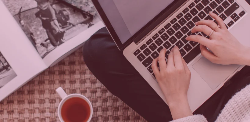 Na stoliku stoi laptop, obok którego widać kubek z herbatą oraz magazyn