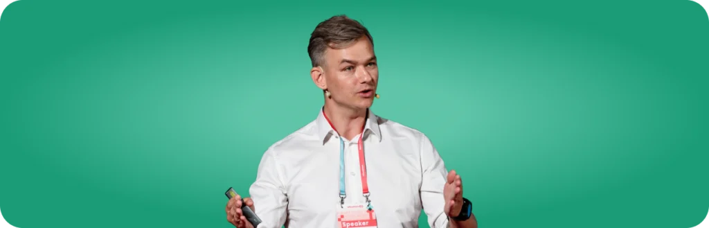 Olaf leśniak na zielonym tle i w białej koszuli mówi coś do widowni