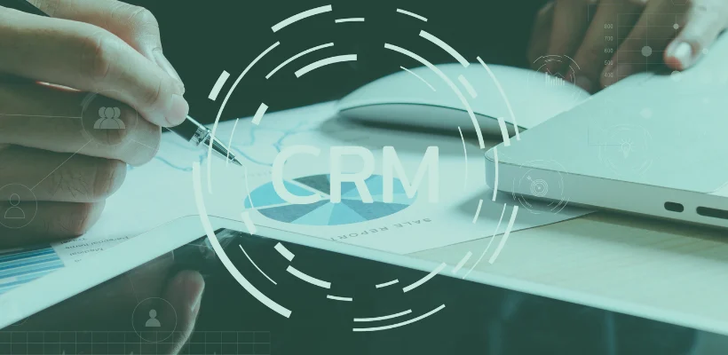 Na ekranie widać stół z tabletem i wykresami oraz napis CRM